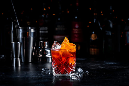 Cóctel Negroni en vaso bajo con cáscaras de naranja, hielo y fondo oscuro.